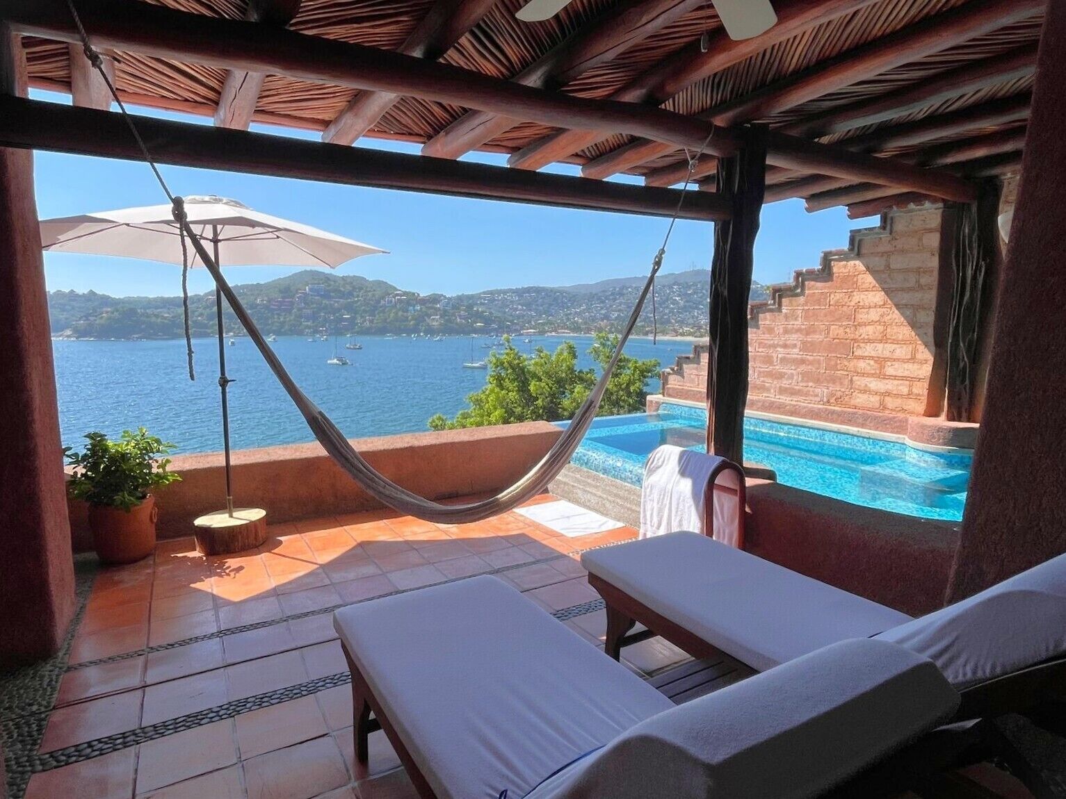 A poolside area with a hammock, lounge chairs, and a view of the sea.
