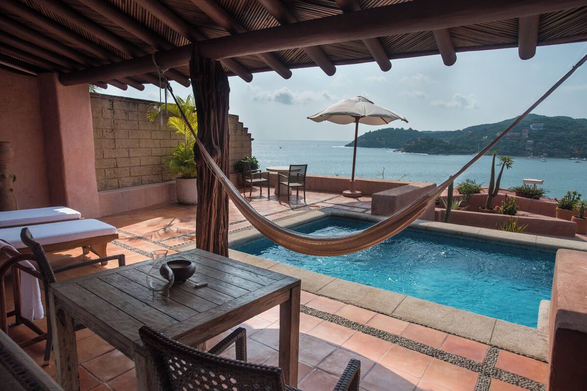 A poolside area with a hammock, lounge chairs, and a view of the sea.