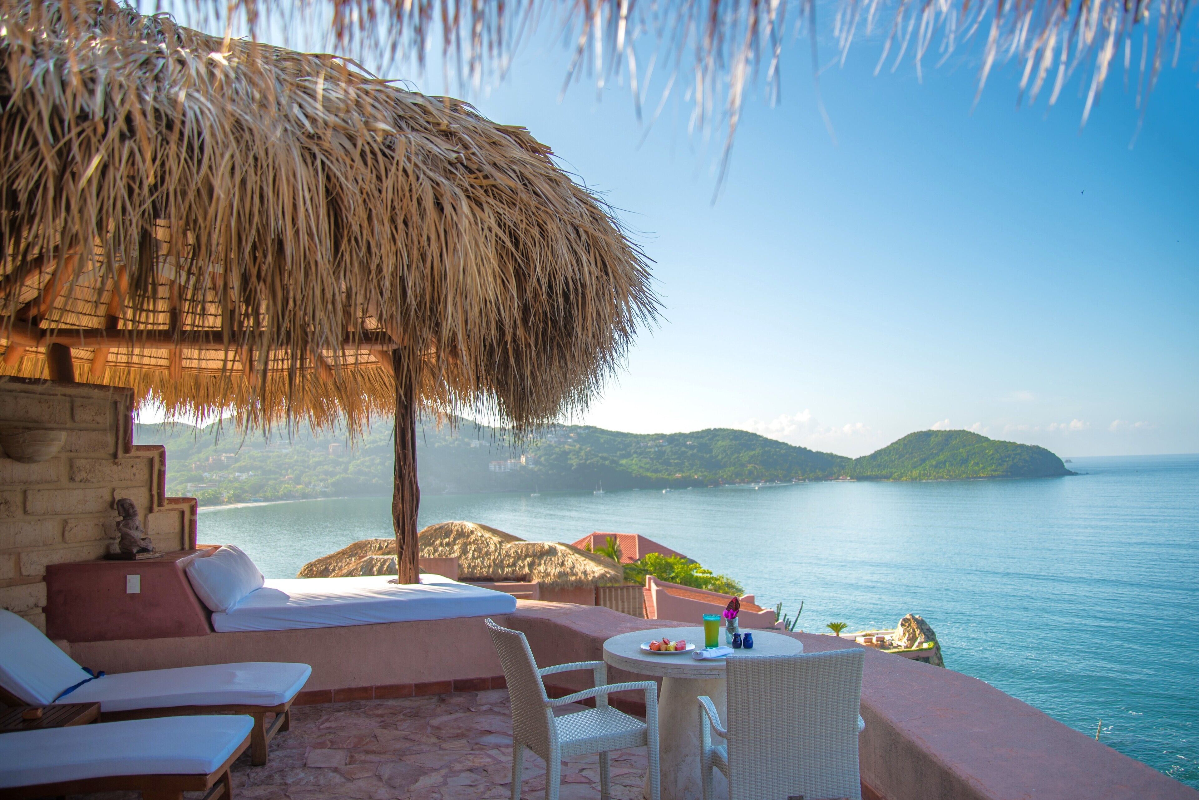 A seaside terrace with a thatched roof, a stone wall, and a view of the sea.