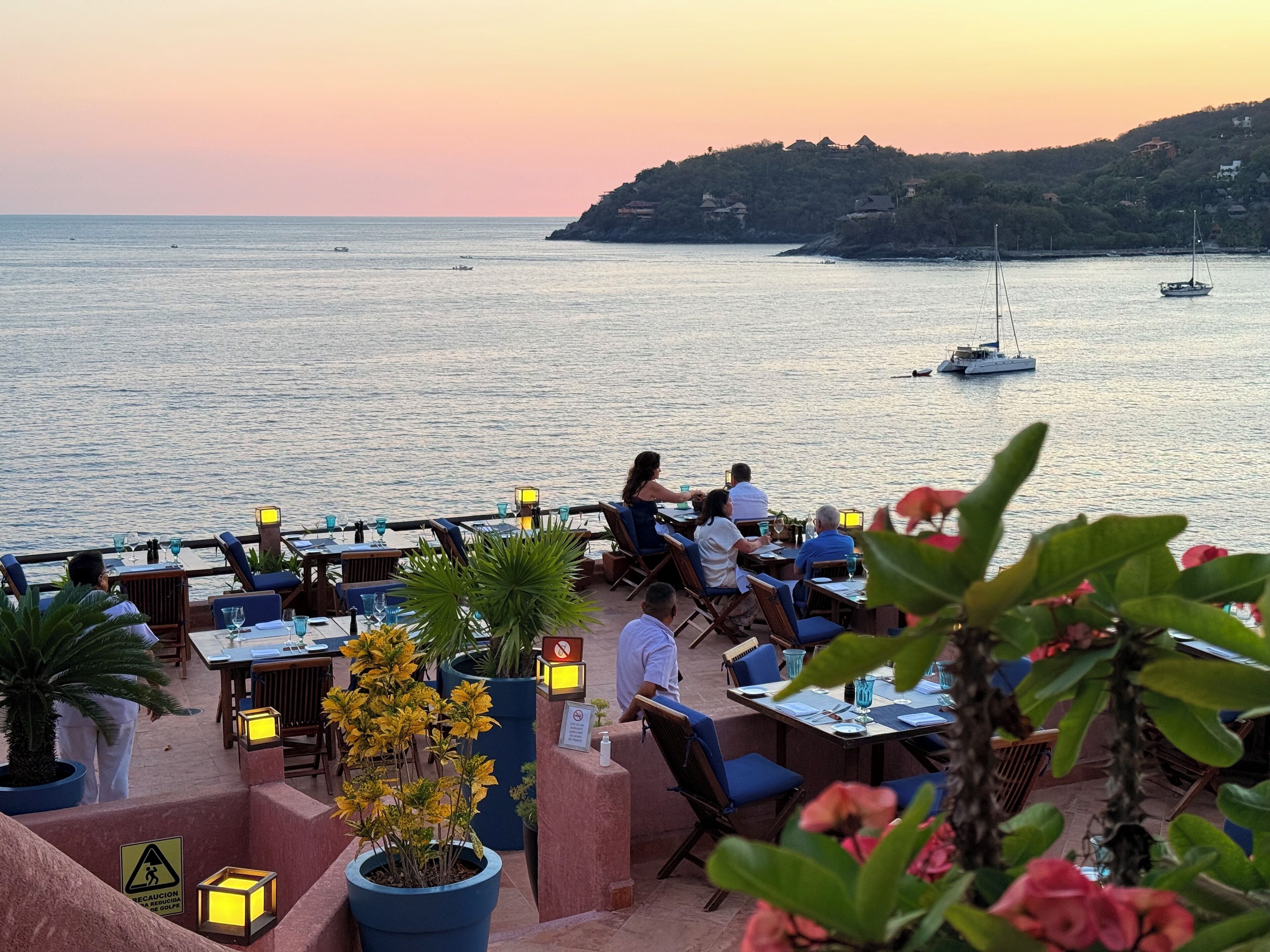 Ein Restaurant am Meer mit Außenbereich und Meerblick, mit Tischen, Stühlen und Blumentöpfen.
