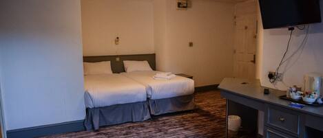 A hotel room with two beds, a desk, a television, and a trash bin.