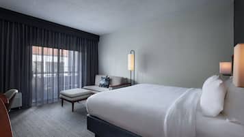 A hotel room with a large bed, a desk, a chair, and a window with curtains.