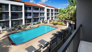 A hotel with a swimming pool, outdoor seating, and palm trees.