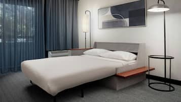 A modern hotel room with a bed, a bedside table, a lamp, and a window with curtains.