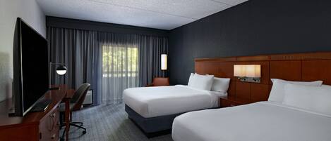 A hotel room with two beds, a desk, a TV, and a window with curtains.
