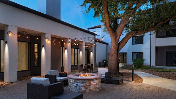 An outdoor patio with a stone fire pit, wicker furniture, and string lights.