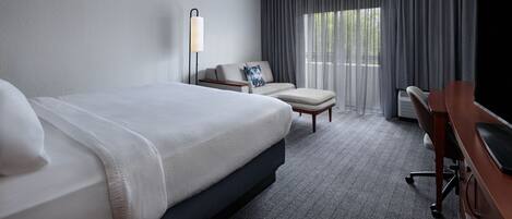 Une chambre d’hôtel avec un grand lit, un bureau, une chaise, une lampe et un téléviseur.