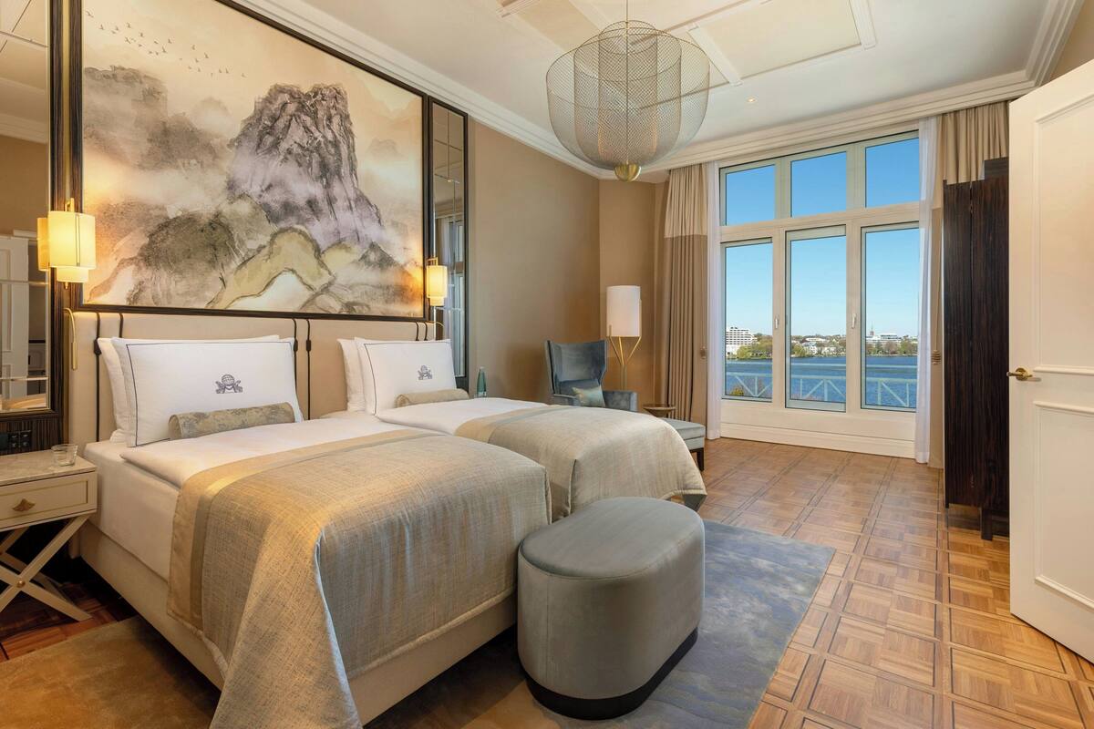 Habitación de hotel con dos camas, un cuadro grande, vistas de la ciudad y un ventanal amplio.