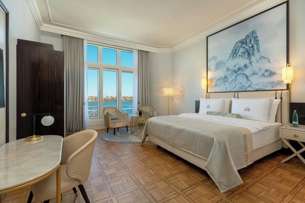 Habitación de hotel con una cama grande, un escritorio, una silla, vista al mar y un cuadro en la pared.
