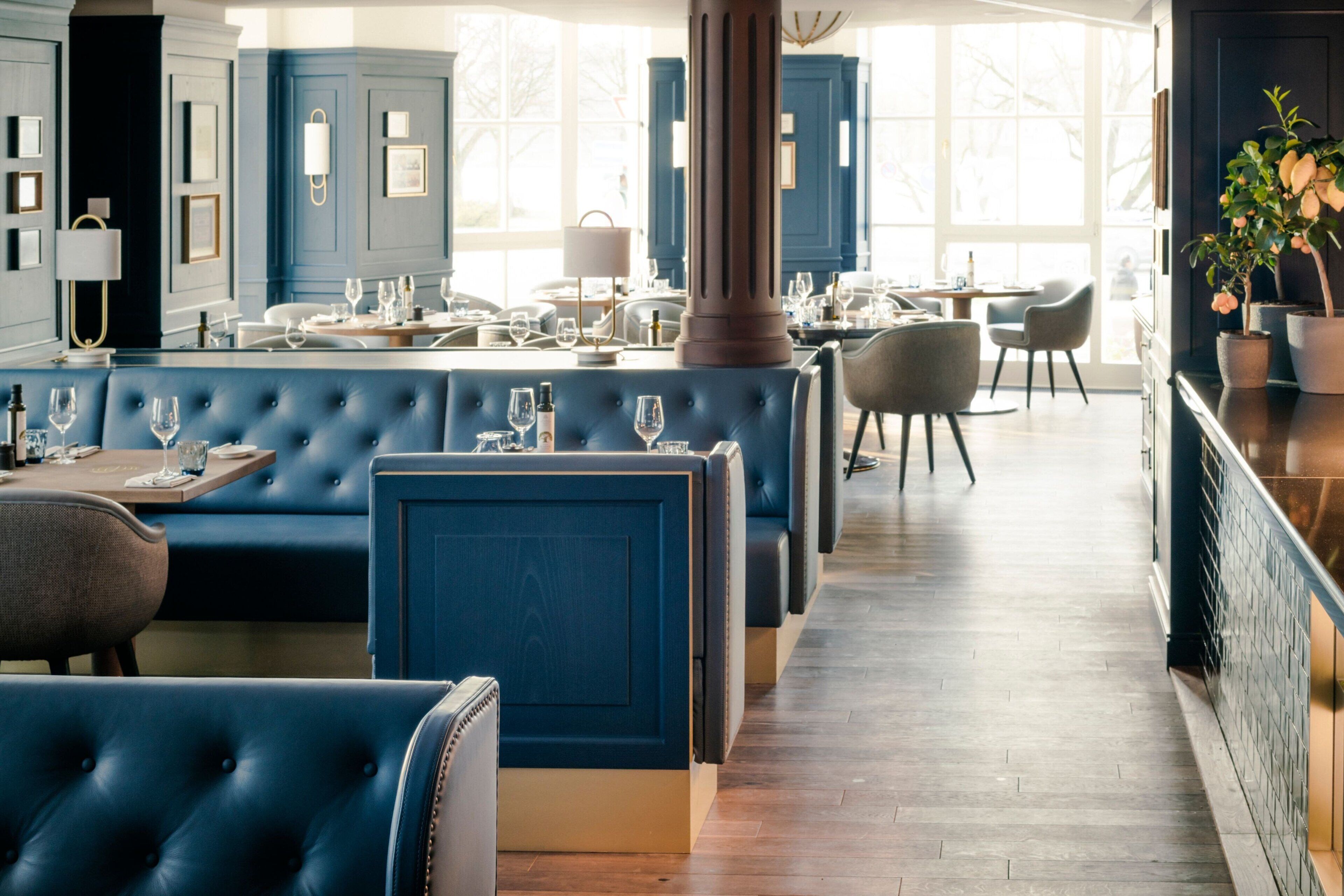 Un ristorante con sedute imbottite blu, pavimento in legno e ampie finestre.