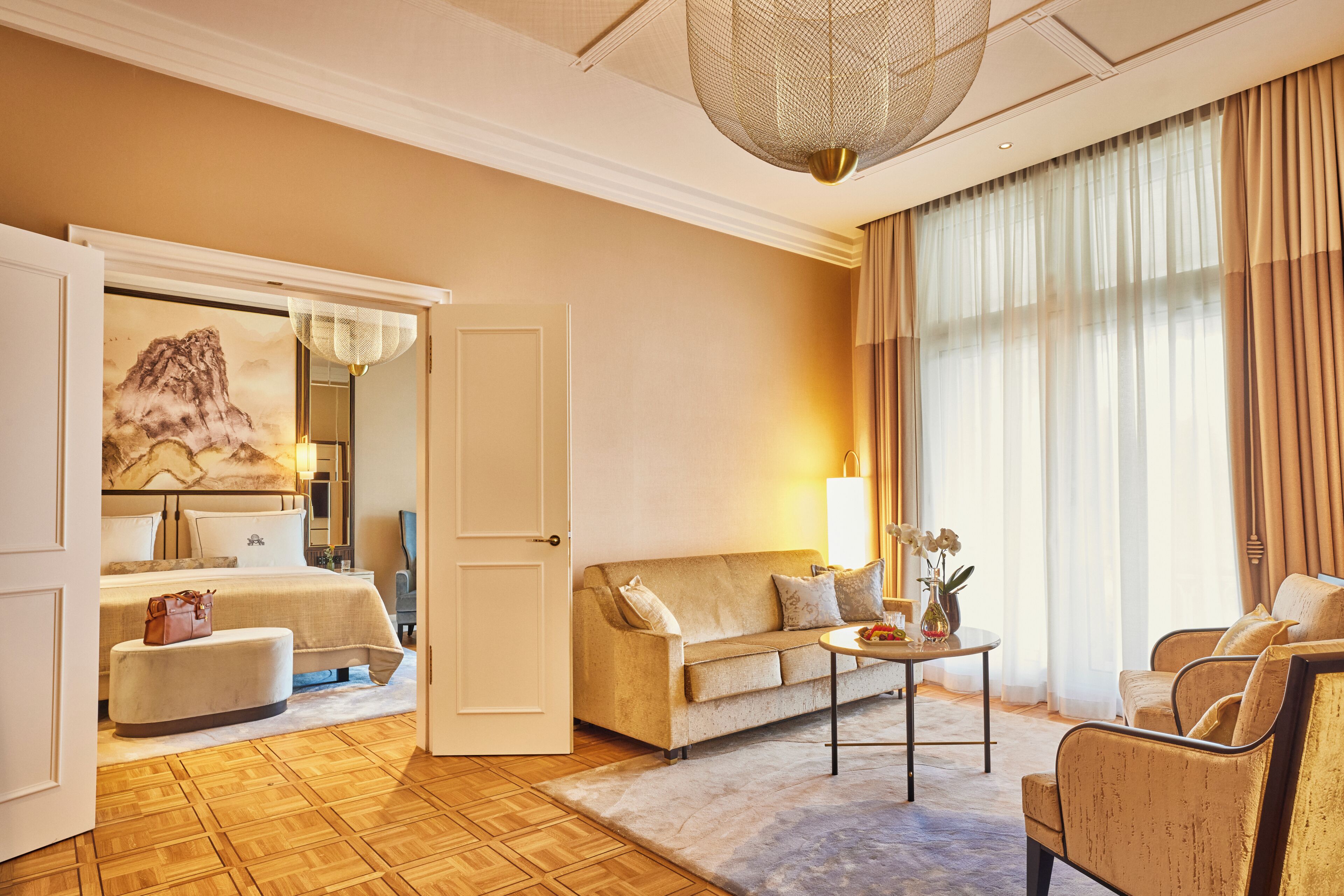 Una habitación de hotel con cama, sofá, mesa de centro y un ventanal con cortinas.