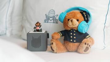 A teddy bear with headphones and a toy figure on a bed.