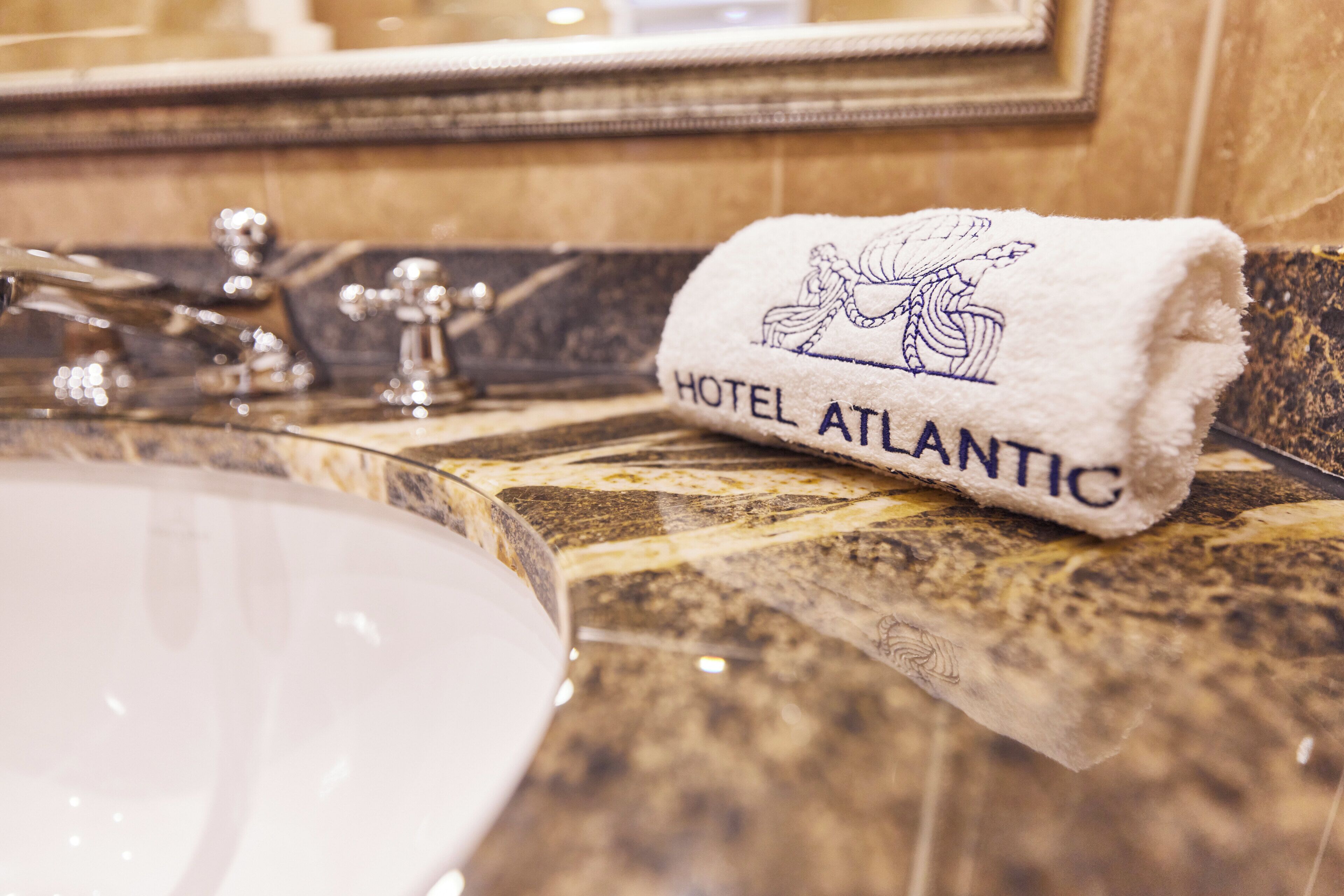 Une salle de bain avec un comptoir en marbre, un lavabo et une serviette brodée avec le nom « HÔTEL ATLANTIC ».