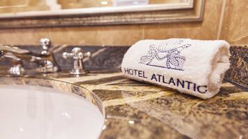 Une salle de bain avec un comptoir en marbre, un lavabo et une serviette brodée avec le nom « HÔTEL ATLANTIC ».