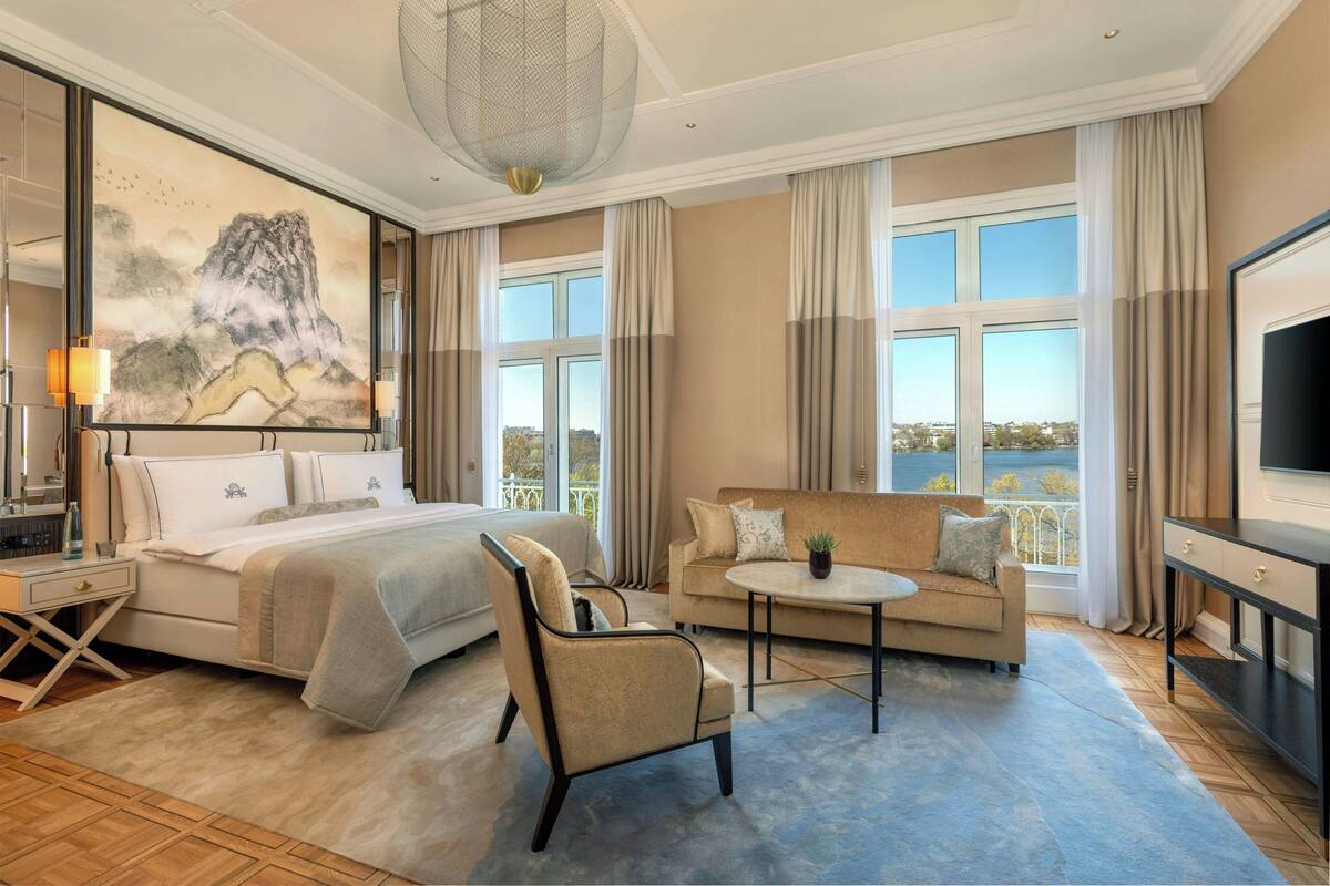 Habitación de hotel con cama, sofá, sillón, una mesita, televisión y un cuadro en la pared.