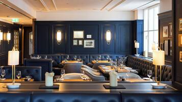A formal dining area with dark wood paneling, multiple seating arrangements, and wall-mounted lighting fixtures.