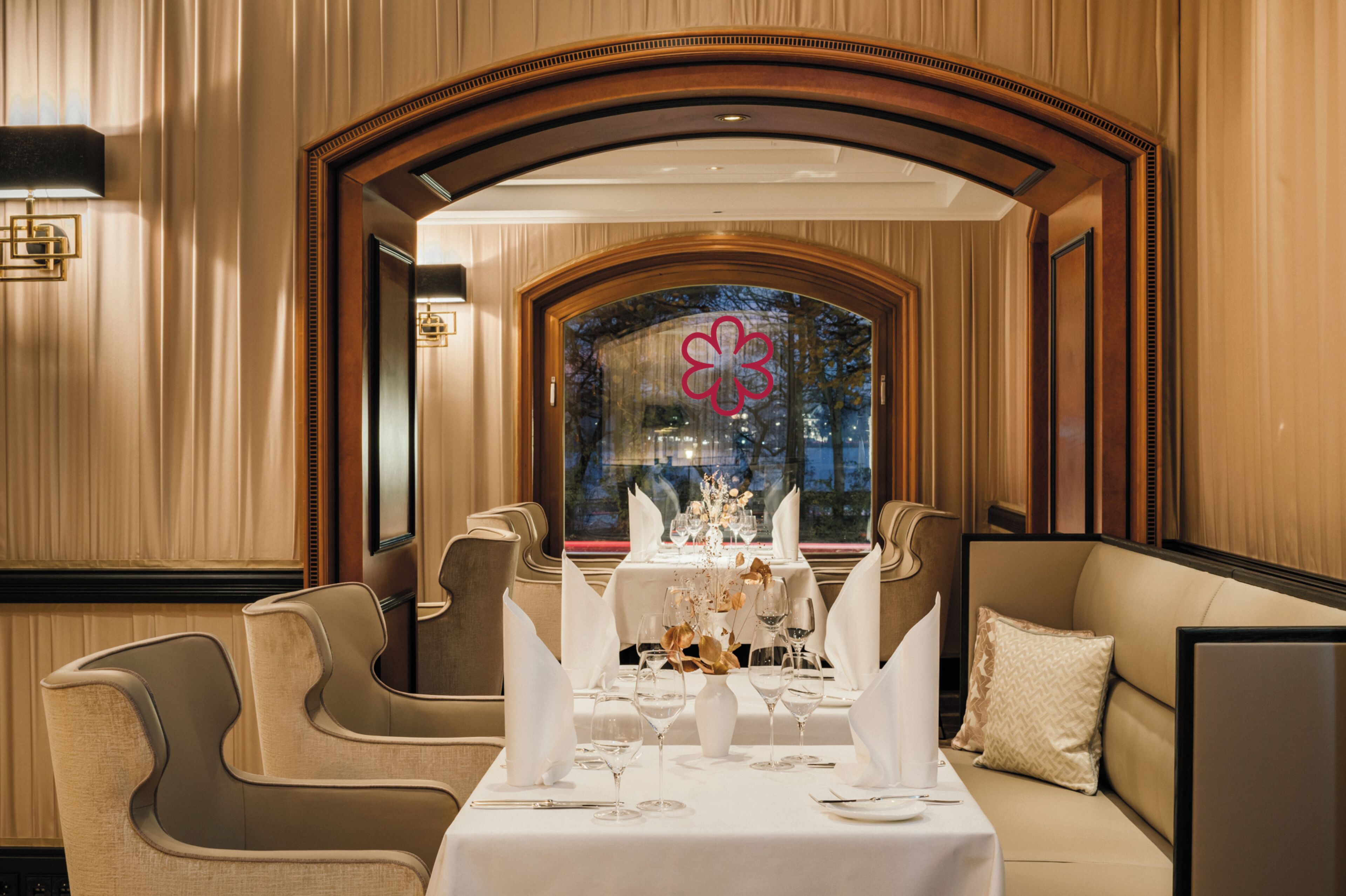 Zona pranzo con tavolo apparecchiato per due, sedie eleganti e vista attraverso una finestra con un elemento decorativo.