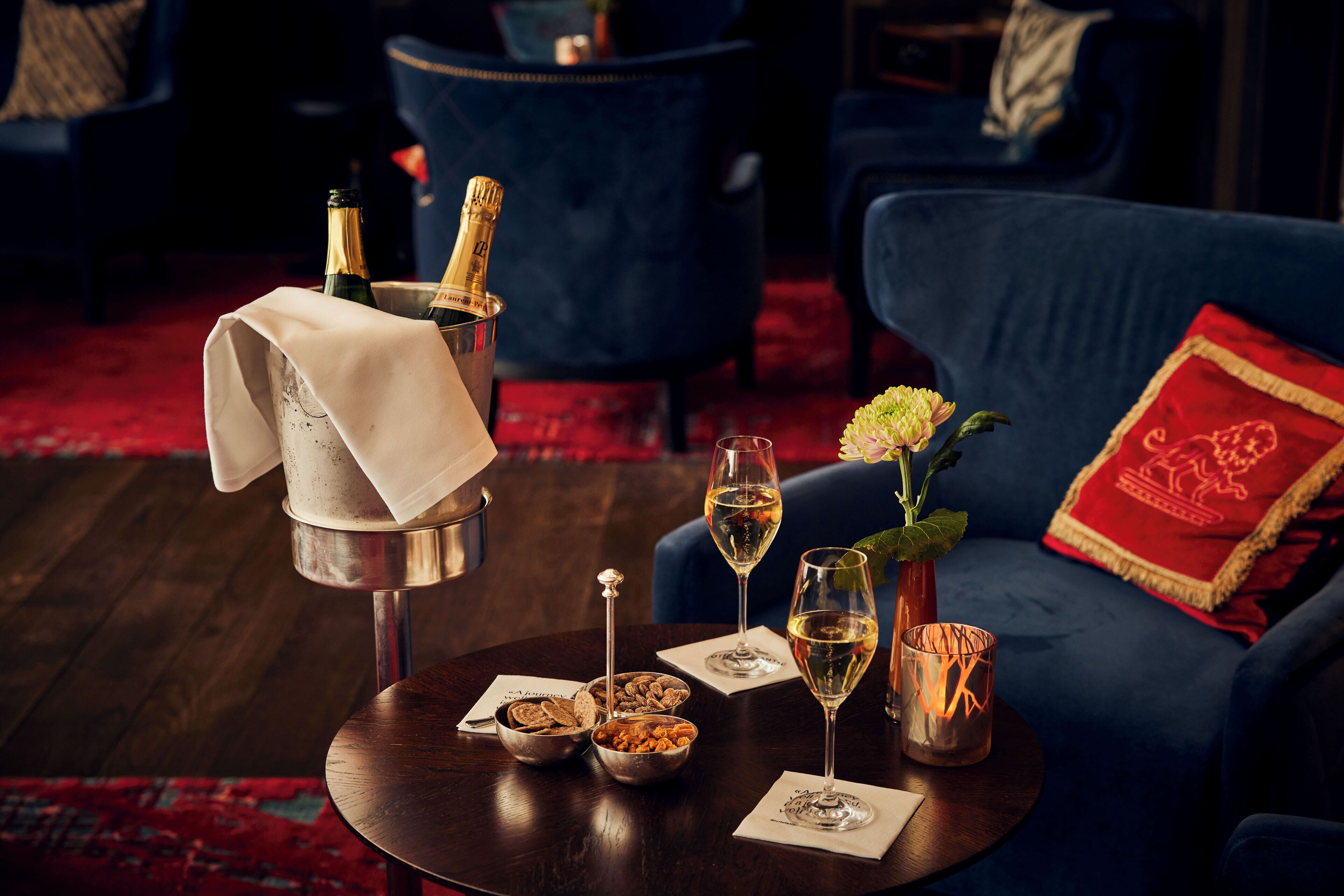 Een tafel met champagne, twee wijnglazen, een kaars en een schaal met noten.