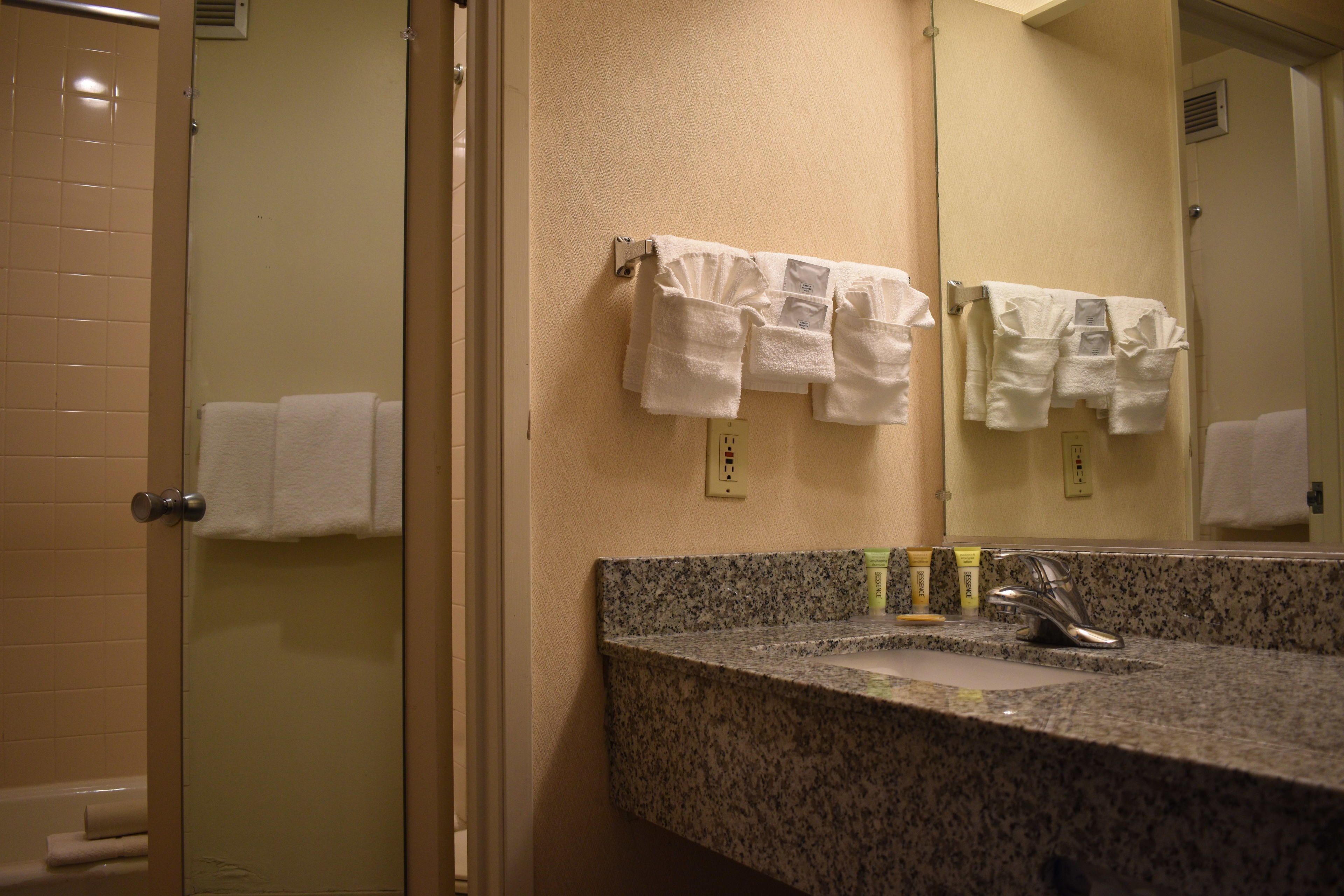 A bathroom with a granite countertop, a sink, and a mirror. There are towels hanging on a rack and a towel dispenser.