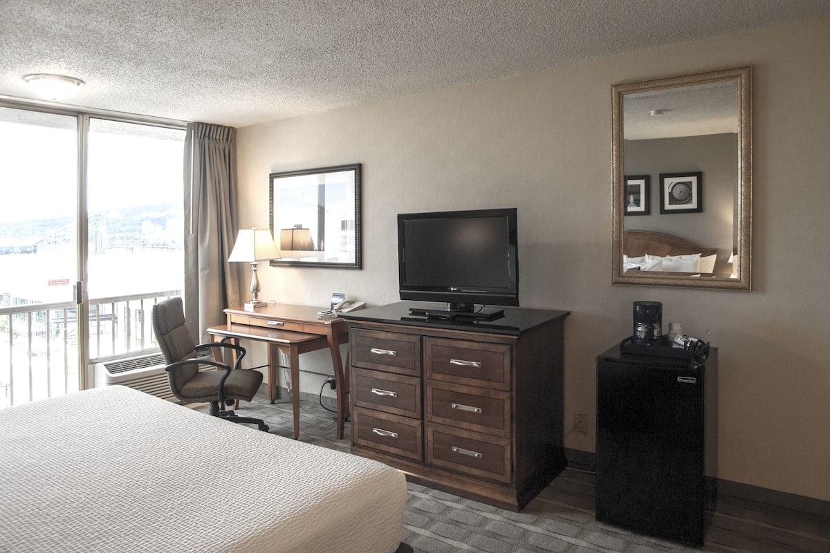 A hotel room with a bed, desk, chair, television, dresser, and a large mirror.