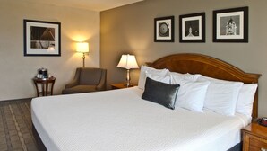 Une chambre d’hôtel avec un grand lit, deux tables de chevet, une chaise et trois tableaux encadrés au mur.