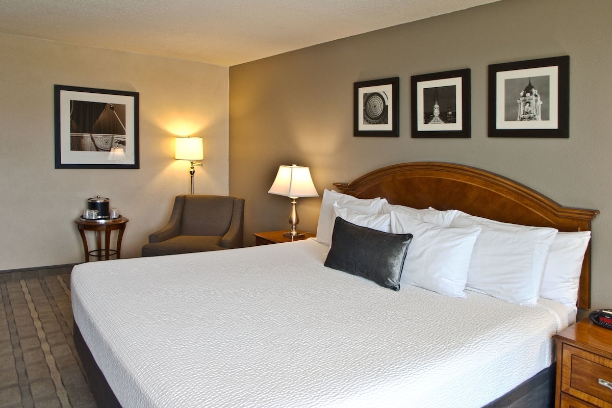 A hotel room with a large bed, two bedside tables, a chair, and three framed pictures on the wall.