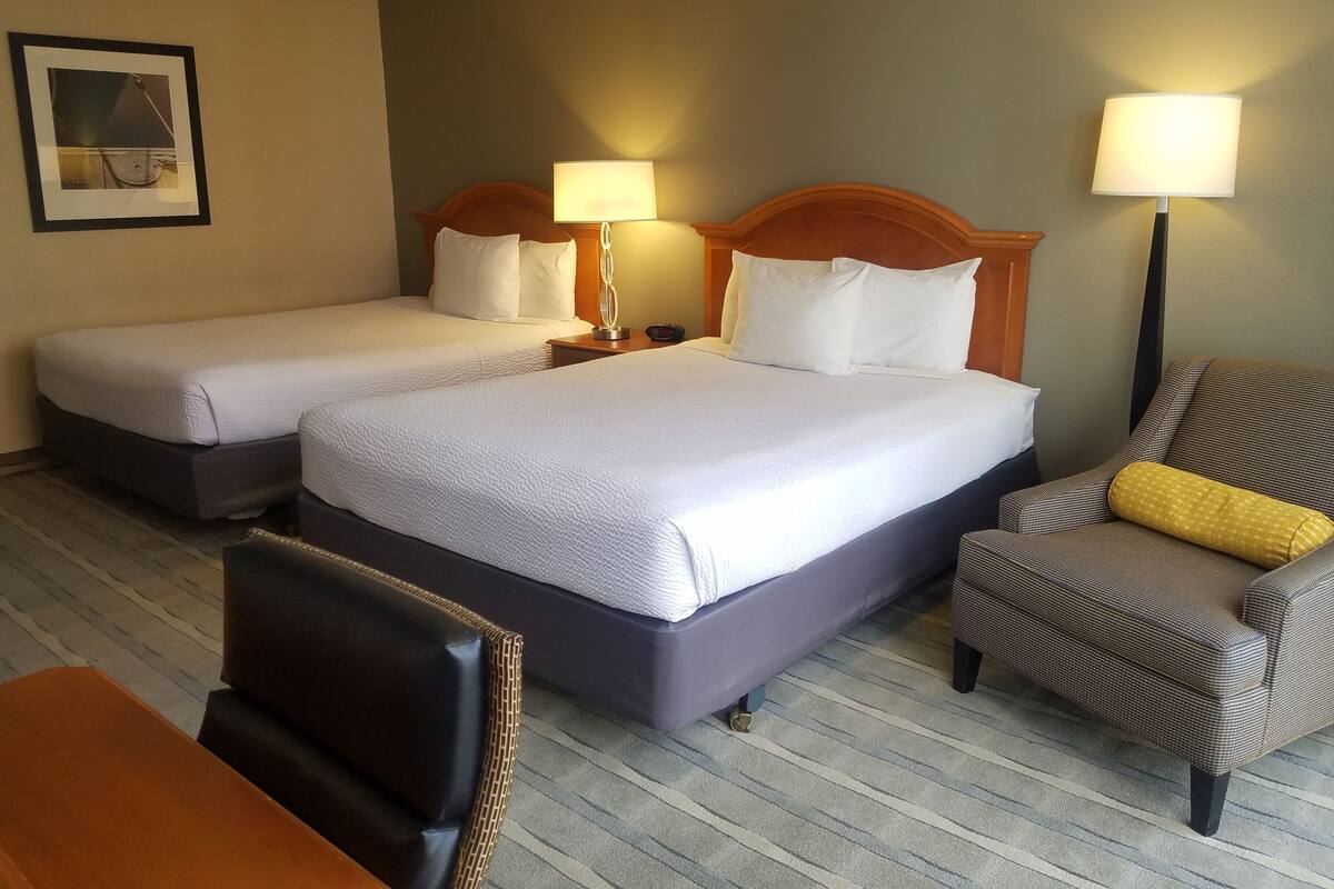 A hotel room with two beds, a chair, a desk, and a lamp.