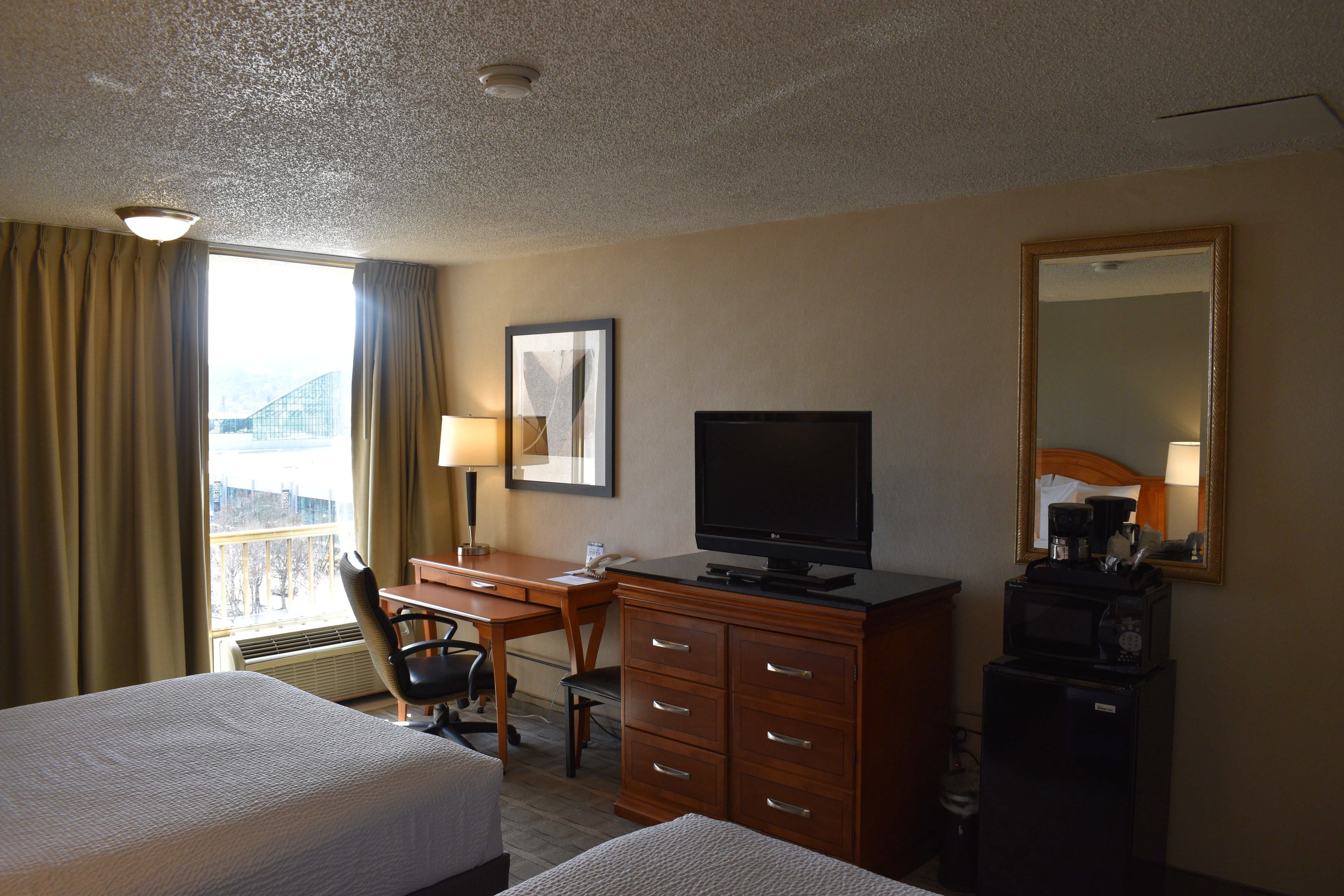 A hotel room with a bed, a desk with a computer, a television, a dresser, and a mirror.
