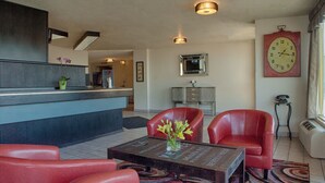 Un hall d’entrée avec un comptoir de réception, deux fauteuils en cuir rouge, une table basse avec un vase, une horloge et un téléphone d’époque.