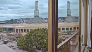 Une vue d’un bâtiment doté de deux hautes tours, une structure moderne en verre, et d’un arbre au premier plan.