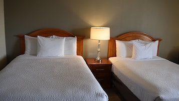 Dos camas individuales con cabeceras de madera, una mesita de noche con lámpara y una pared de color neutro.