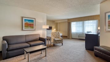 A hotel room with a sofa, armchair, desk, and a large window with curtains.