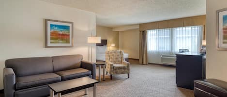 Une chambre d’hôtel équipée d’un canapé, d’un fauteuil, d’un bureau et d’une grande fenêtre avec des rideaux.