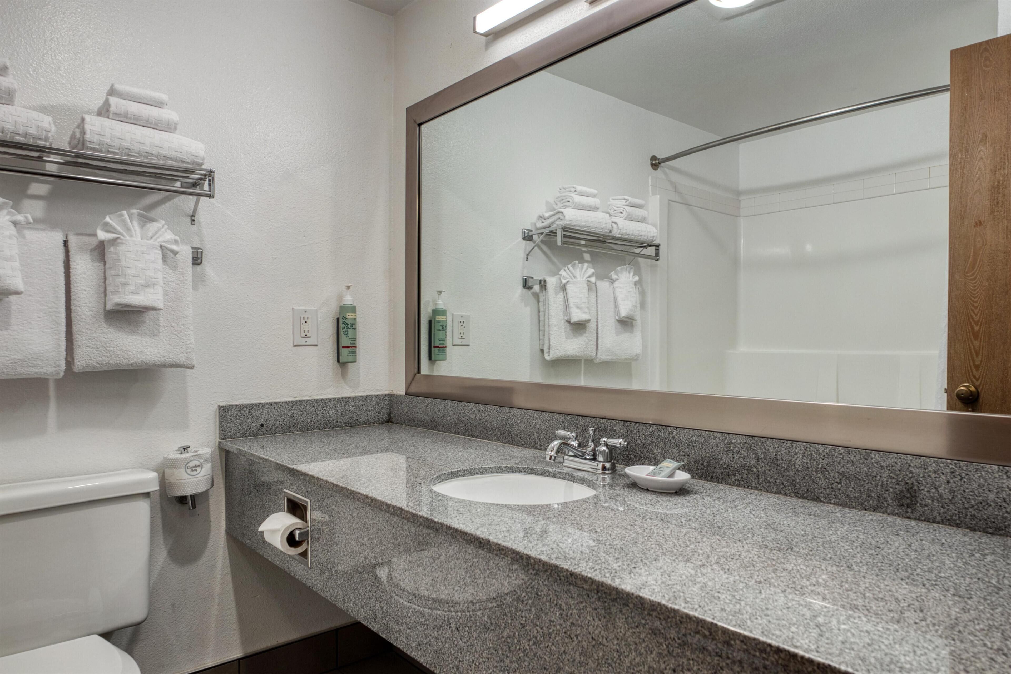 A bathroom with a sink, mirror, towel rack, toilet, and toiletries.