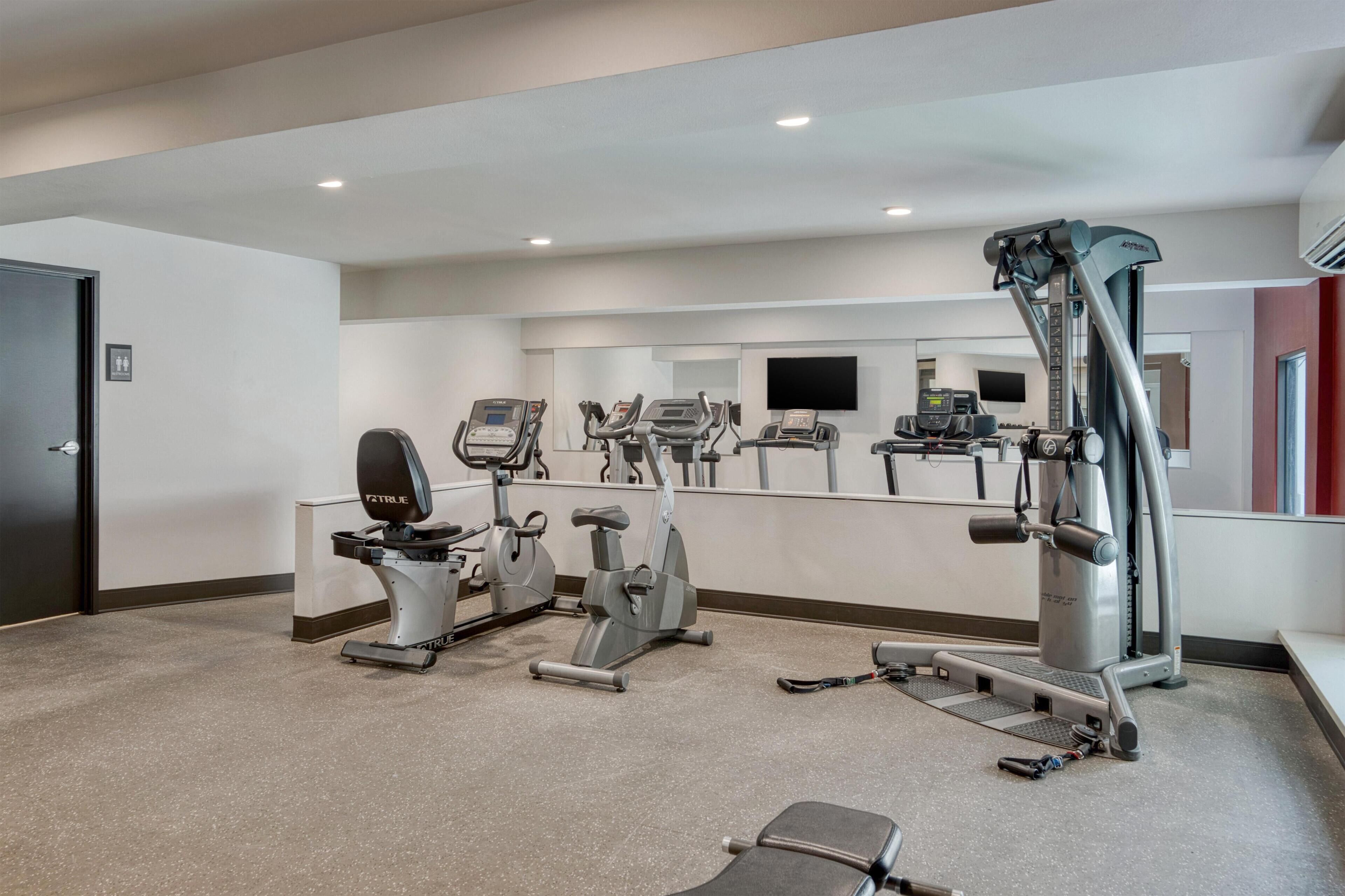 Une salle de sport équipée de divers appareils pour le cardio et le renforcement musculaire, notamment des tapis de course, des vélos d’appartement et une machine de musculation.