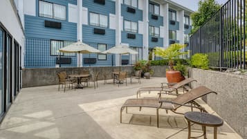 An outdoor patio with lounge chairs and umbrellas, a concrete floor, and a building with blue and white exterior walls.