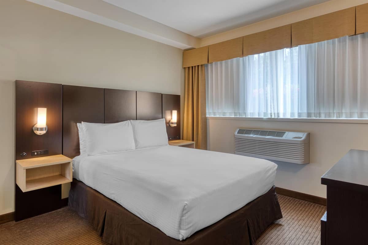 Ein Hotelzimmer mit einem großen Bett, zwei Nachttischen, einer Wandklimaanlage und einem Fenster mit Vorhängen.