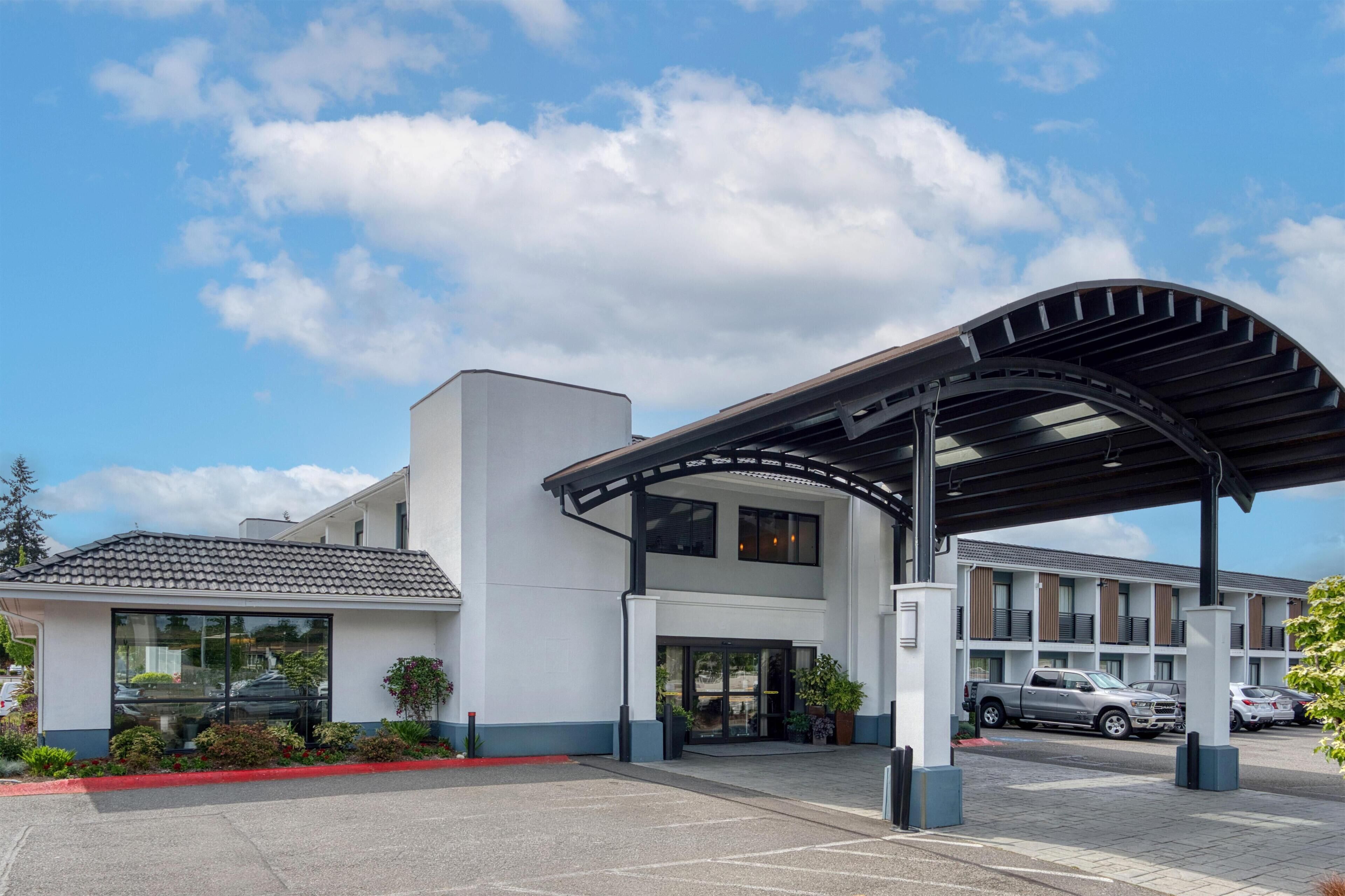 Un edificio moderno con ingresso coperto, un parcheggio e un veicolo sullo sfondo.