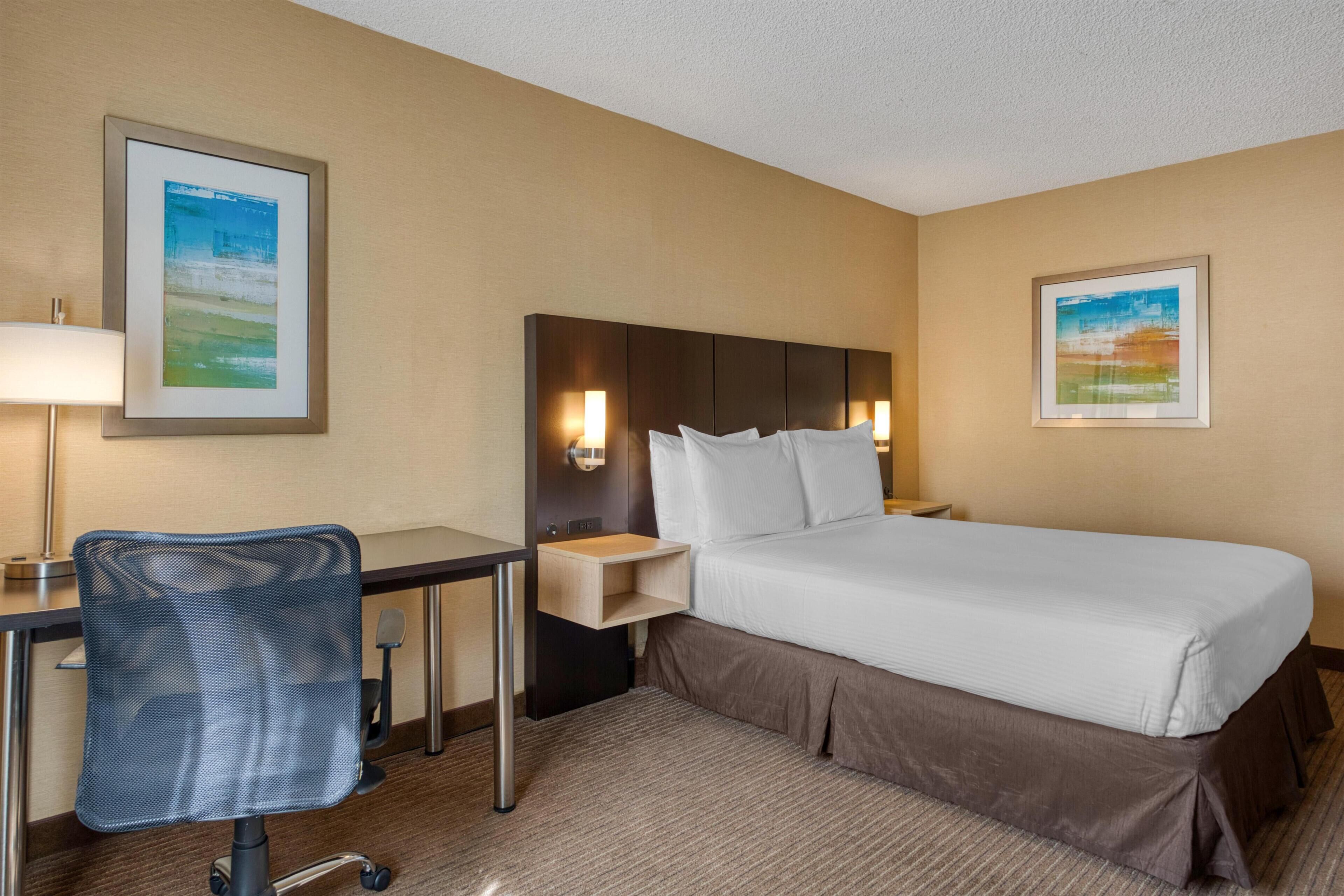 A hotel room with a bed, desk, chair, and two wall-mounted lamps.