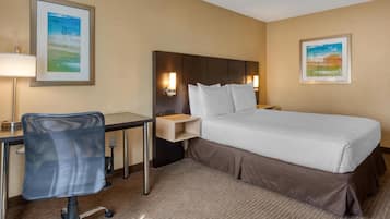 A hotel room with a bed, desk, chair, and two wall-mounted lamps.