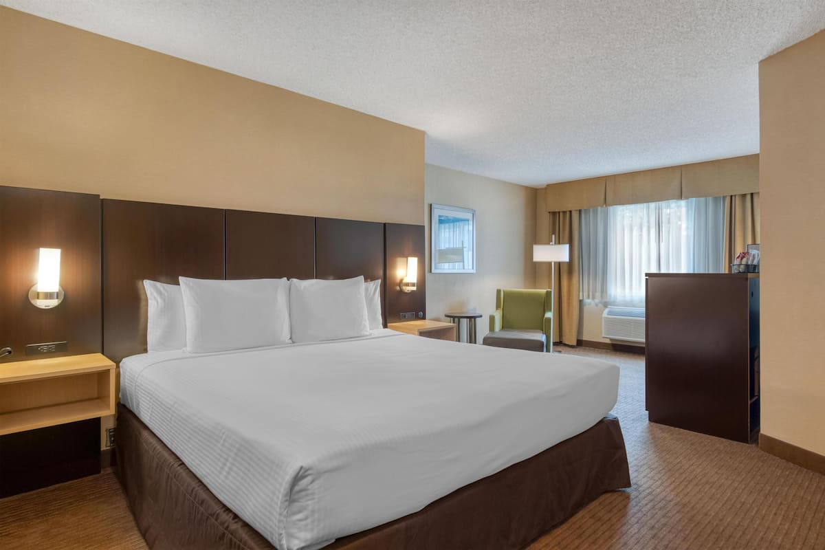 Ein Hotelzimmer mit einem großen Bett, Nachttischen, einem Schreibtisch, einem Sessel und einem Kleiderschrank.