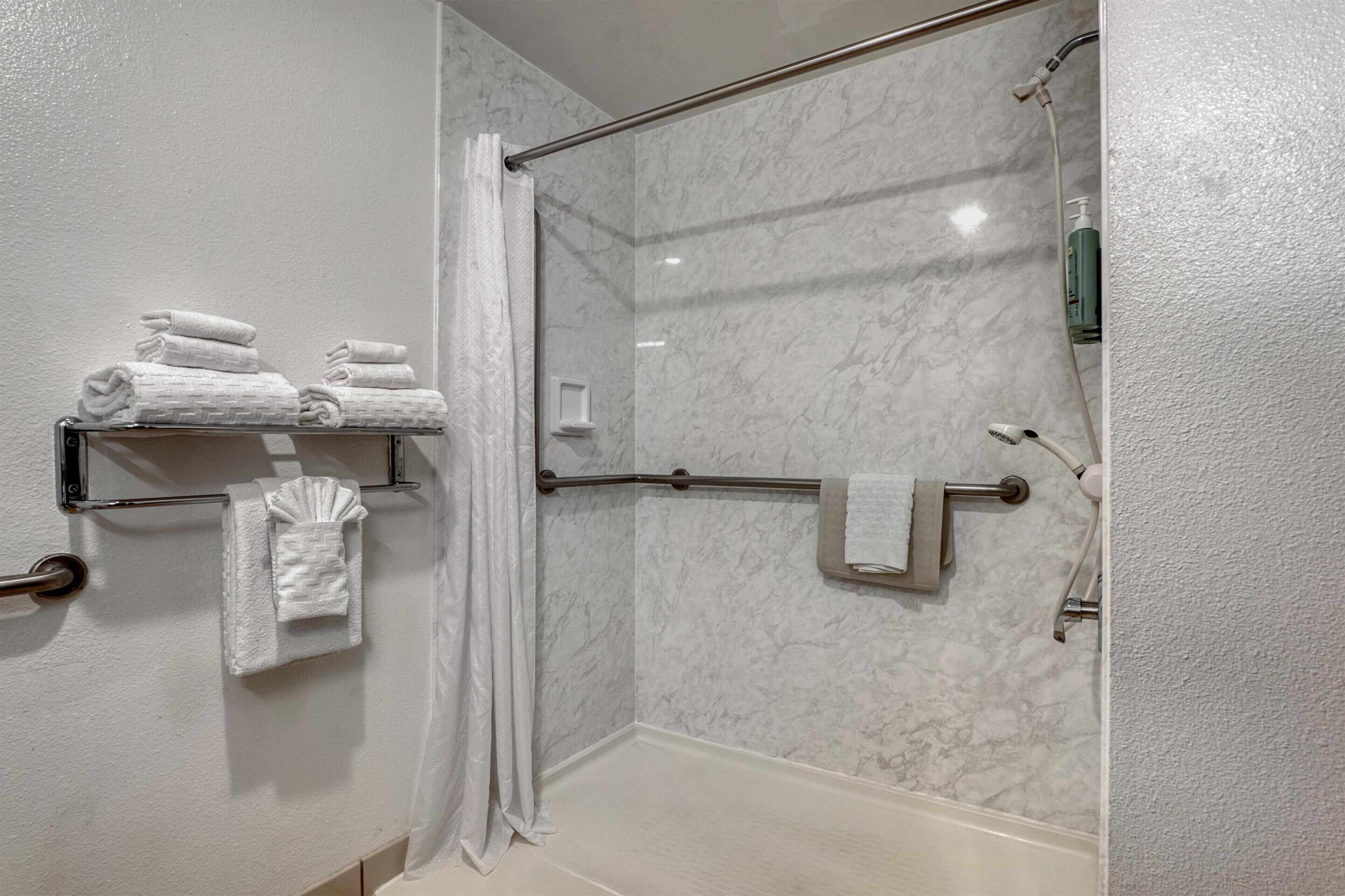 Un espace douche doté d’une porte en verre, d’un porte-serviettes avec des serviettes pliées et d’un pommeau de douche.