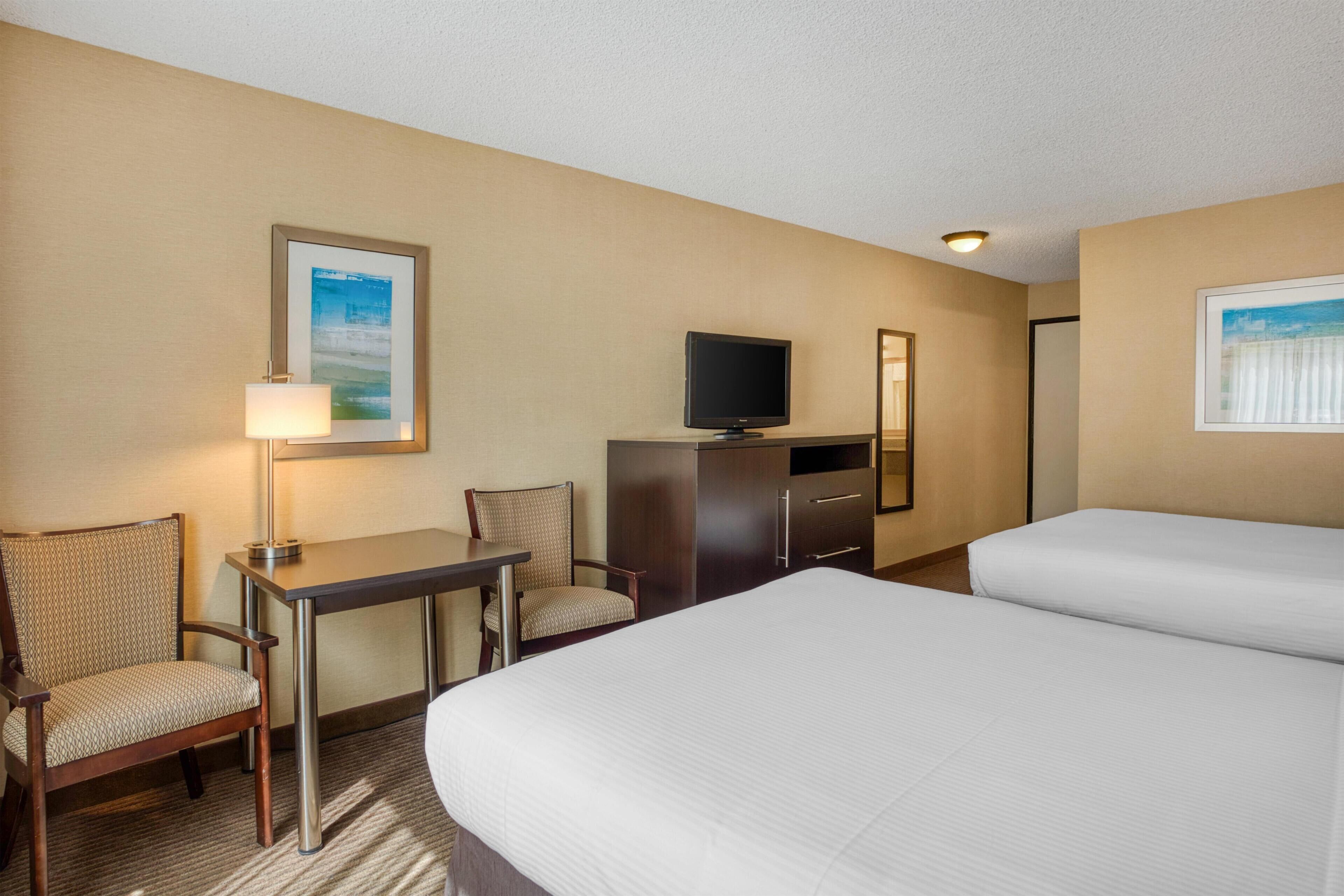A hotel room with two beds, a desk with a chair, a television, and framed pictures on the walls.