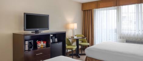A hotel room with two beds, a TV, a desk with a lamp, and a small table with chairs.
