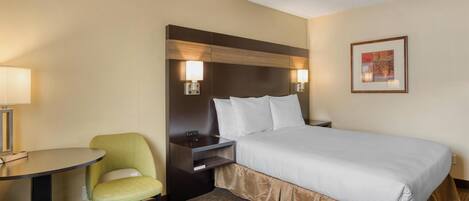 Habitación de hotel con cama, escritorio, dos sillas, mesita de noche y un cuadro enmarcado en la pared.