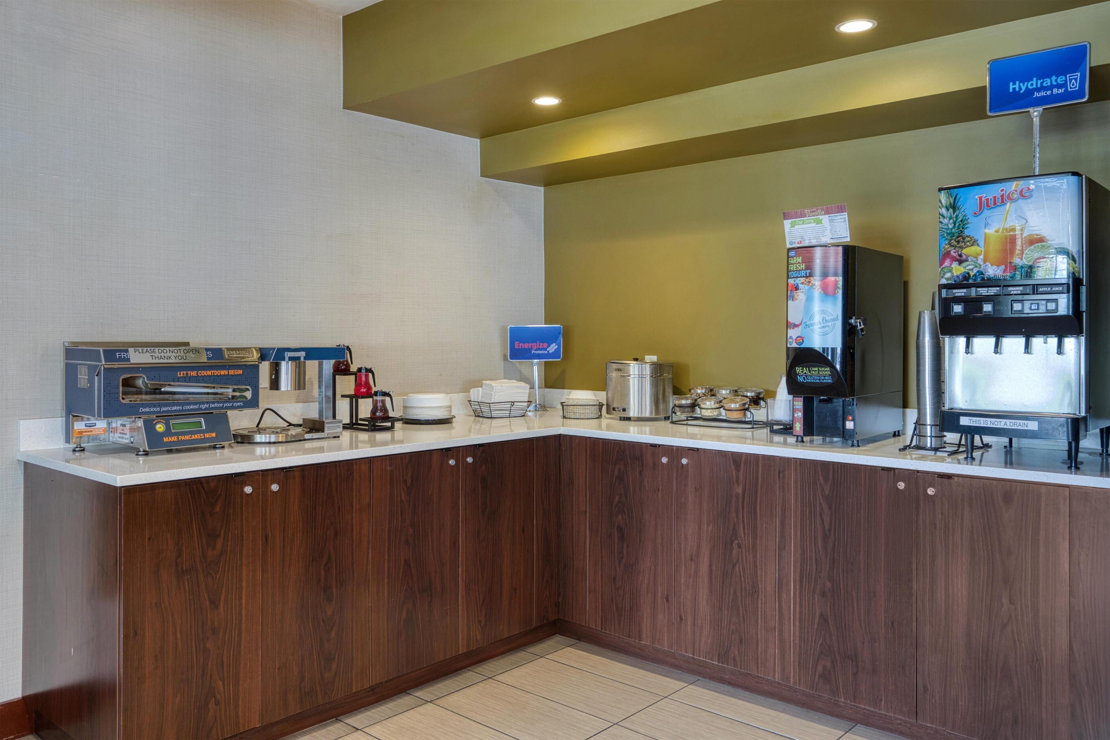 A hotel breakfast area with a juice bar, coffee machine, and a sign for Energise.