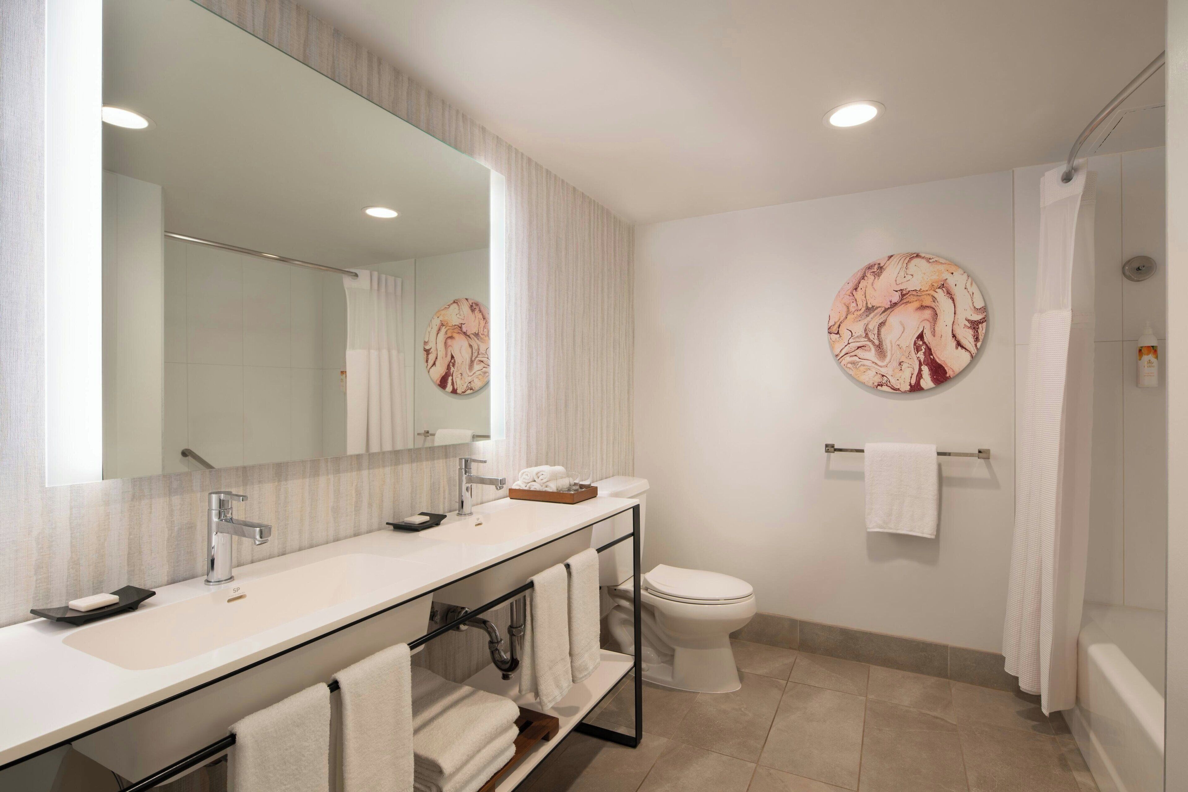 Une salle de bain moderne avec un grand miroir, un lavabo, des toilettes et une douche.
