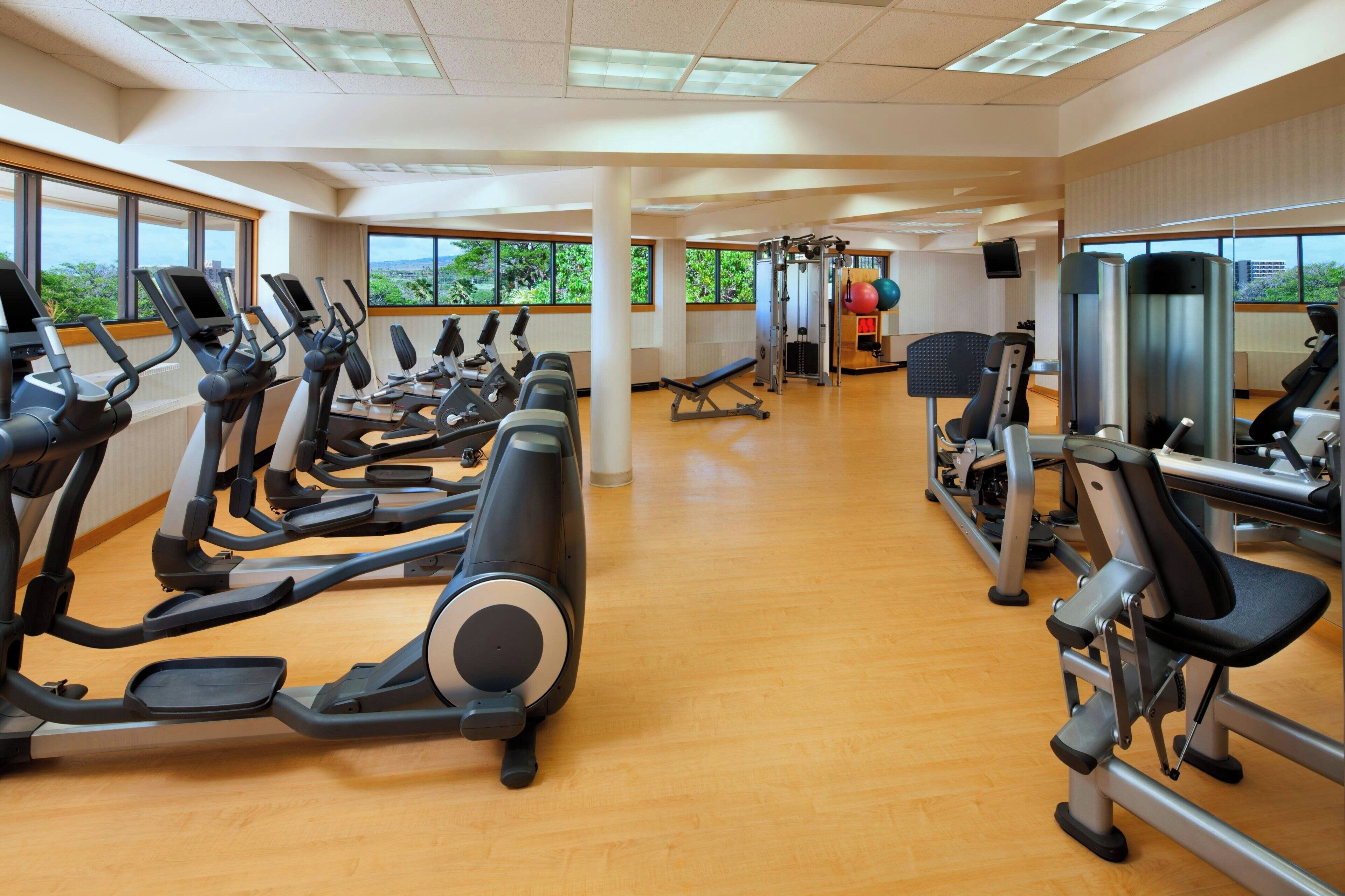 Un gimnasio con cintas de correr, máquinas de pesas y un amplio ventanal con vistas a zonas verdes.