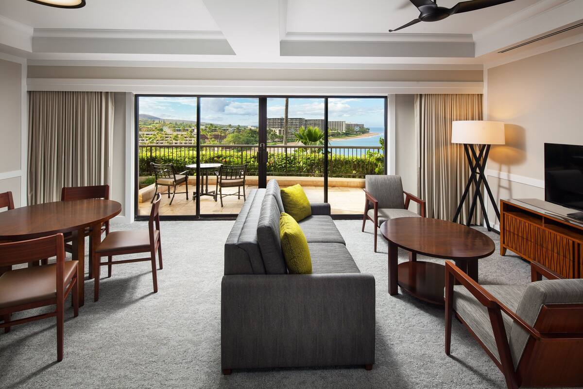 A hotel room with a balcony, a sofa, a dining table, and a TV.