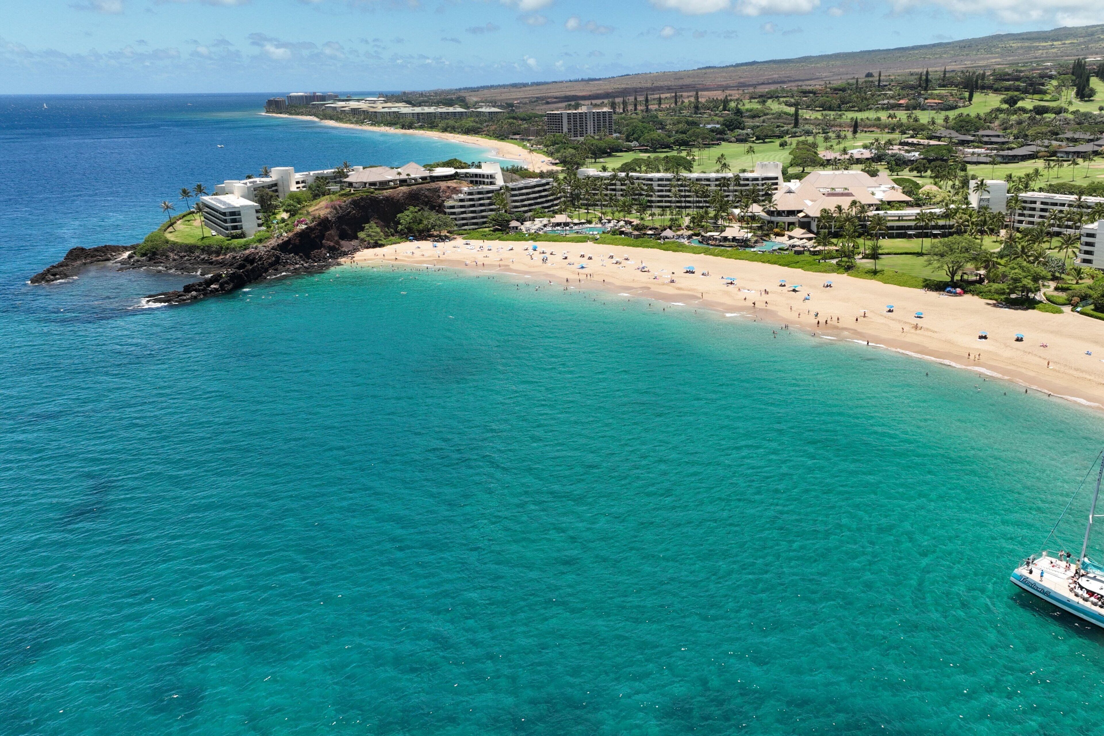 A coastal resort with a beach, clear turquoise waters, and a sailboat.